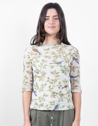 A woman modeling a three-quarter sleeve top with a delicate bird and leaf pattern on a light cream background, paired with olive green pants, against a plain white studio background.