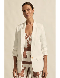 Woman wearing a white blazer over a patterned outfit against a beige background