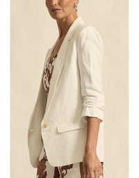 Woman wearing a white blazer over a patterned dress against a beige background