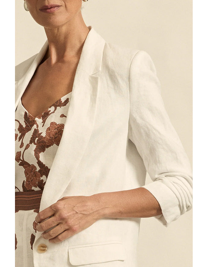 Woman wearing a white blazer over a patterned dress with a neutral background