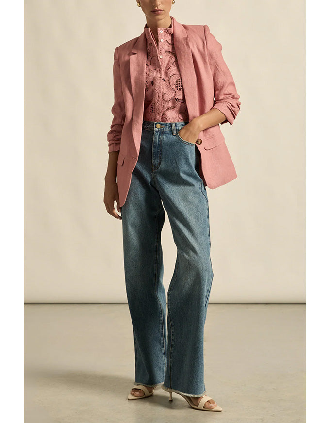 Person wearing a pink blazer and blue jeans on a neutral background
