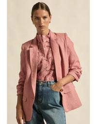 Woman wearing a pink blazer over a patterned shirt with blue jeans on a beige background