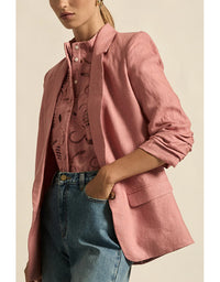 Person wearing a pink blazer over a patterned shirt with blue jeans on a beige background