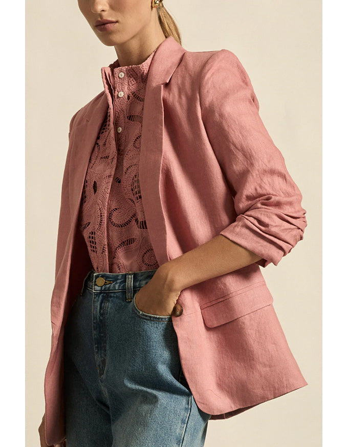 Person wearing a pink blazer over a patterned shirt with blue jeans on a beige background