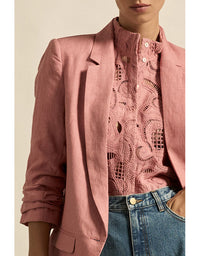 Person wearing a pink blazer over a patterned shirt with blue jeans on a beige background