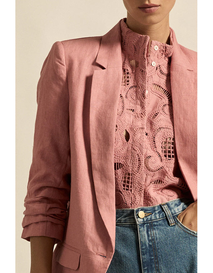 Person wearing a pink blazer over a patterned shirt with blue jeans on a beige background