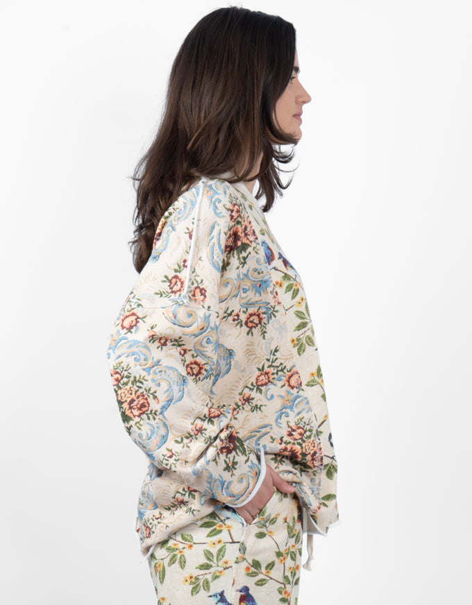 A woman shown in side profile wearing a cream-colored, long-sleeved top with a detailed multicolor floral and ornamental pattern, paired with matching patterned bottoms, against a plain white background.