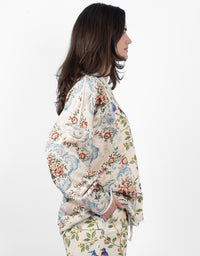 A woman shown in side profile wearing a cream-colored, long-sleeved top with a detailed multicolor floral and ornamental pattern, paired with matching patterned bottoms, against a plain white background.