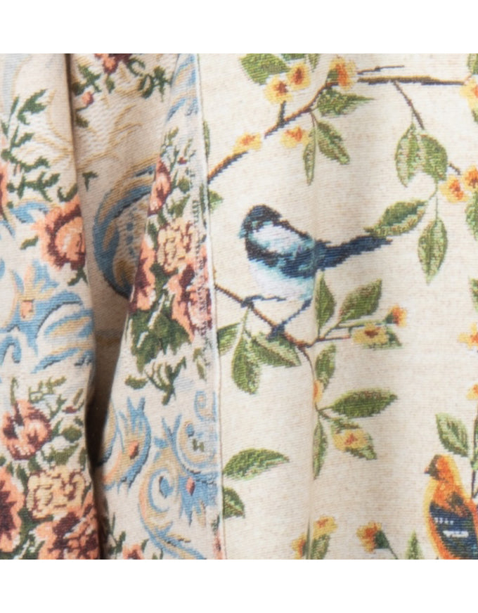 Close-up of a woven textile with a floral and bird pattern on a light beige background, showing branches with green leaves, small yellow flowers, and blue-and-black birds.