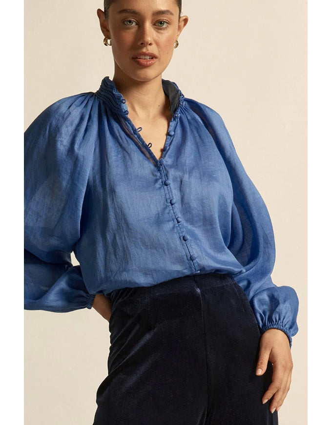 Woman wearing a blue blouse with puffed sleeves against a beige background