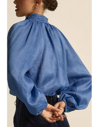 Person wearing a blue blouse with puffed sleeves on a beige background