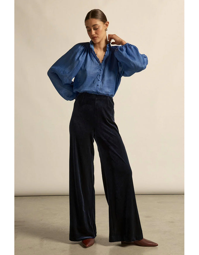 Woman wearing a blue blouse and black pants against a beige background