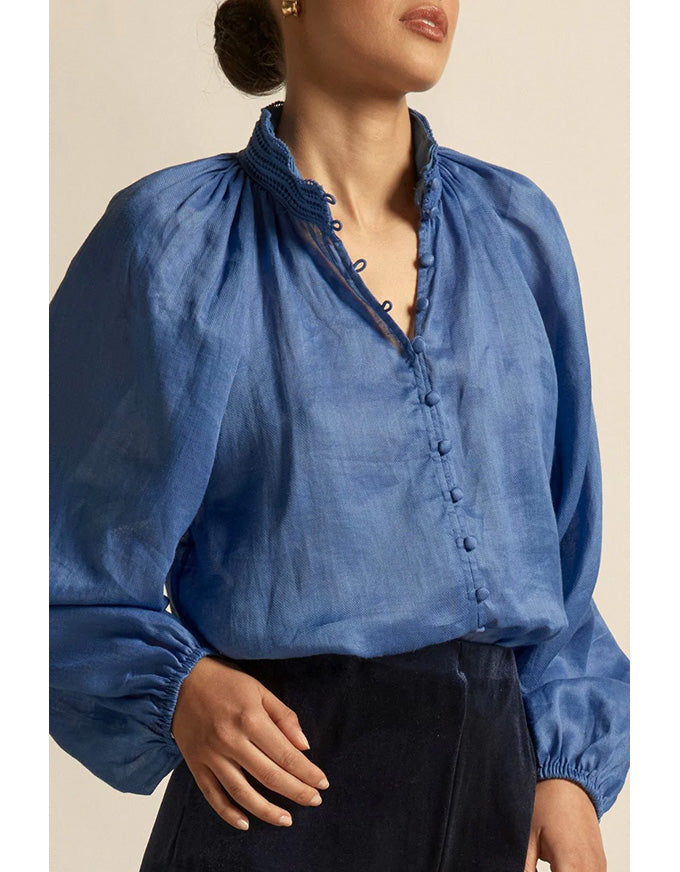 Woman wearing a blue blouse with long sleeves and a high collar against a beige background