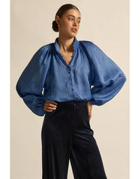 Woman wearing a blue denim blouse with wide sleeves against a beige background
