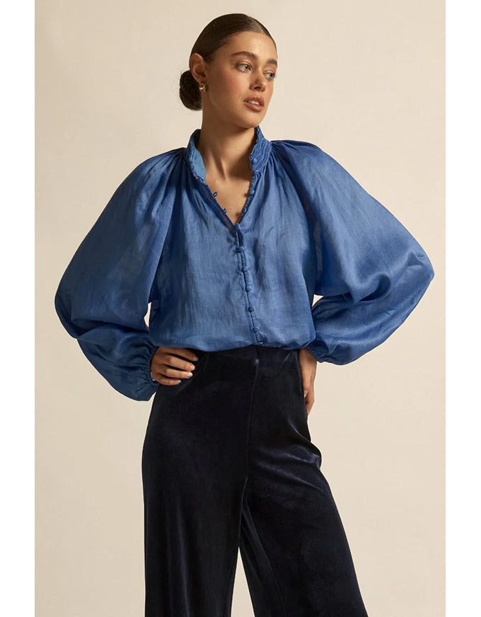 Woman wearing a blue denim blouse with wide sleeves against a beige background
