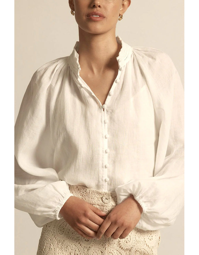 Person wearing a white blouse with long sleeves against a neutral background