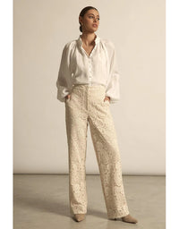 Woman wearing a white blouse and beige patterned pants against a plain background