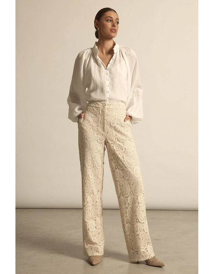 Woman wearing a white blouse and beige patterned pants against a plain background