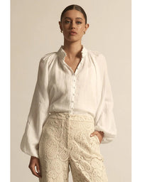 Woman wearing a white blouse and beige lace pants against a neutral background