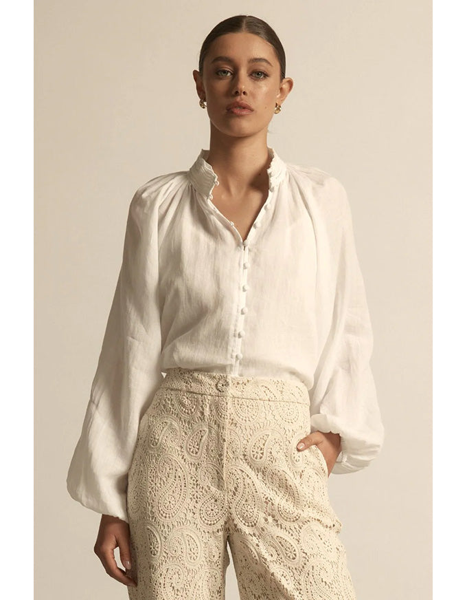 Woman wearing a white blouse and beige lace pants against a neutral background