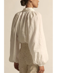 Person wearing a white blouse with long sleeves and a textured beige skirt against a neutral background