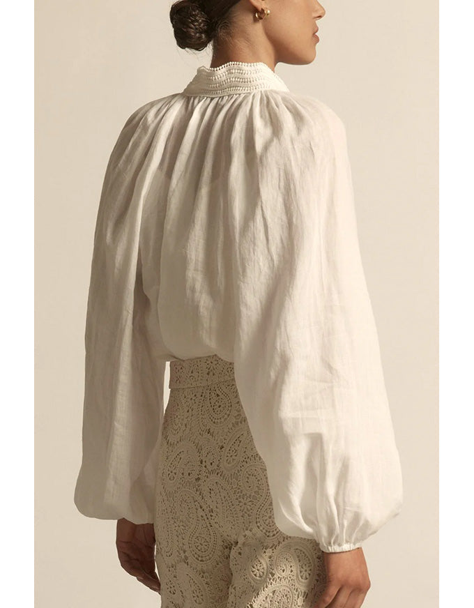Person wearing a white blouse with long sleeves and a textured beige skirt against a neutral background