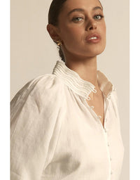 Woman wearing a white blouse with a high collar and buttons, against a neutral background