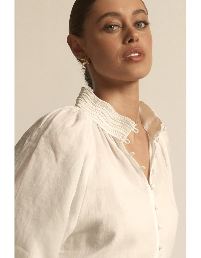 Woman wearing a white blouse with a high collar and buttons, against a neutral background