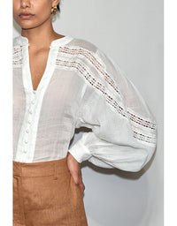 White sheer blouse with lace details worn by a person against a plain background
