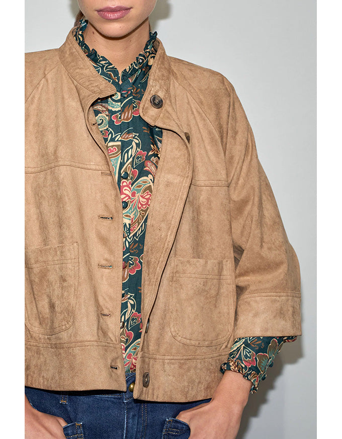 Person wearing a tan jacket over a floral shirt with a plain background