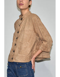 Person wearing a brown suede jacket and blue jeans against a plain background