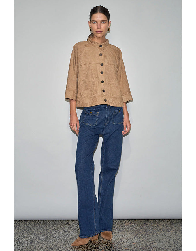 Woman wearing a beige jacket and blue jeans against a plain background