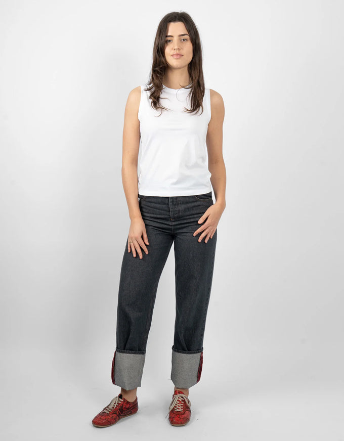 A woman modeling a white sleeveless top, dark gray rolled-calf jeans, and red sneakers against a light gray studio background.