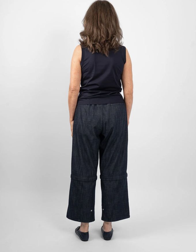 A woman viewed from behind wearing a dark sleeveless top and dark wide-leg cropped pants against a light gray studio background.