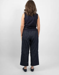 A woman viewed from behind wearing a dark sleeveless top and dark wide-leg cropped pants against a light gray studio background.