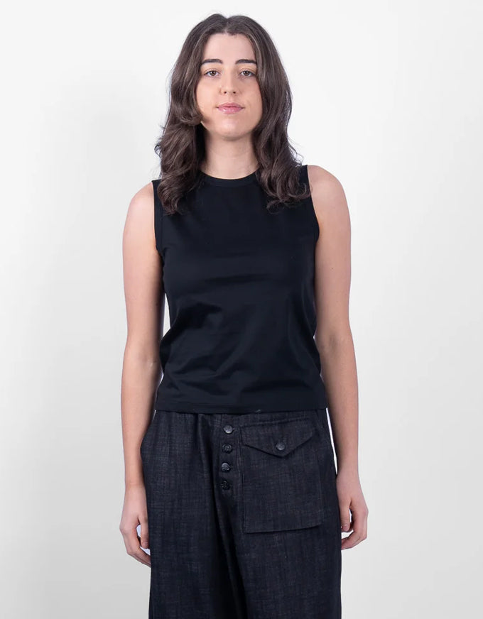 A woman modeling a sleeveless black top and dark charcoal wide-leg pants against a plain light gray studio background.