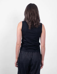A woman viewed from behind wearing a black sleeveless top and dark textured pants against a plain light background.