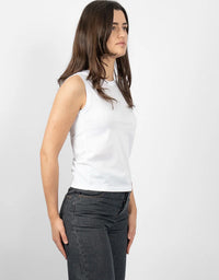 A woman wearing a plain white sleeveless crop top and dark gray jeans, shown from a side profile against a light gray studio background.